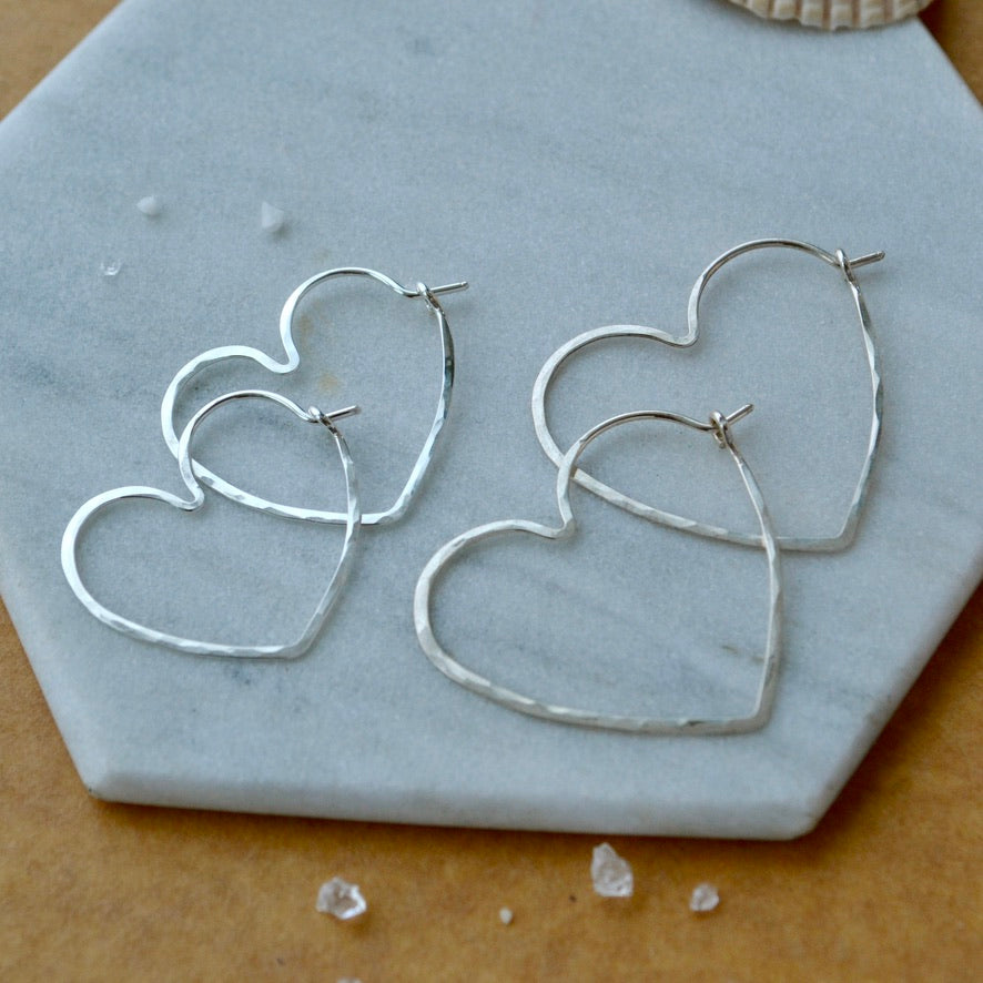 Heart-shaped silver hoop earrings on a marble surface two sizes
