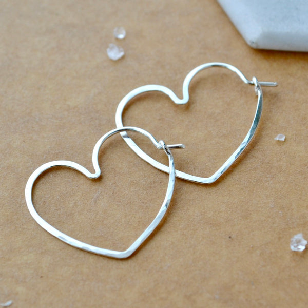 Heart-shaped silver earrings on a beige surface