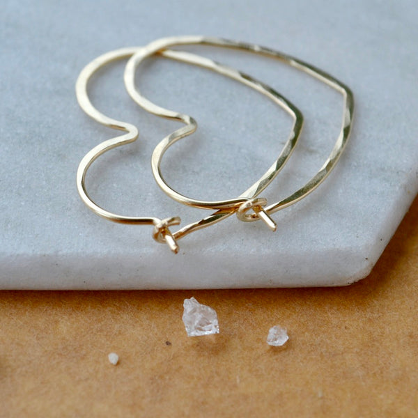 Gold hoop earrings on a marble surface with small crystals.