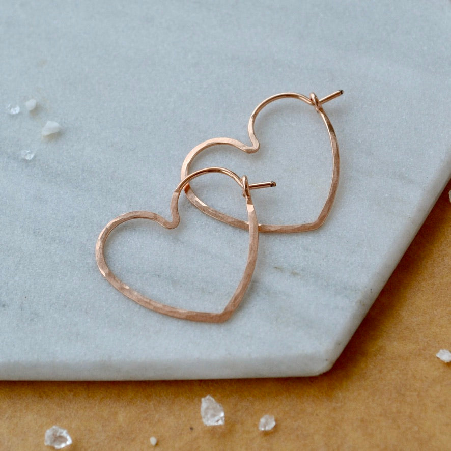 Heart-shaped rose gold earrings on a marble surface with small crystals.