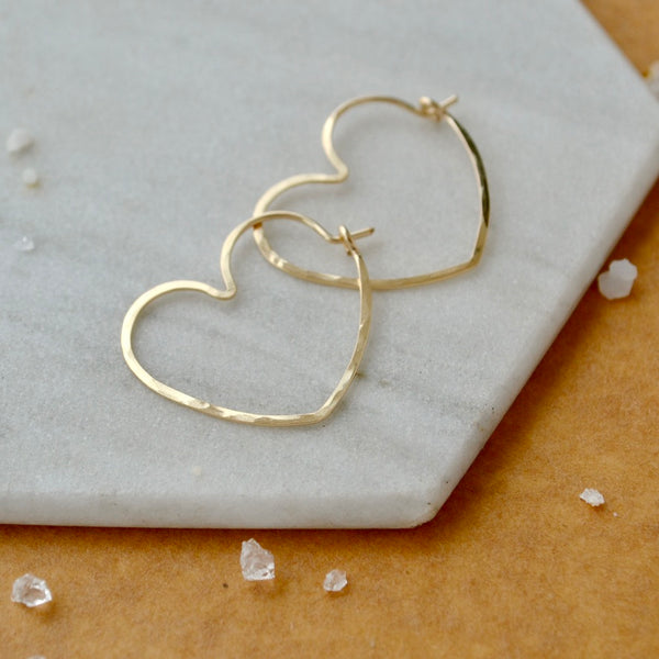 Gold heart-shaped earrings on a light gray surface with small crystals around.