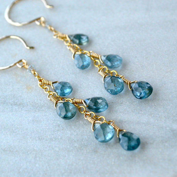 Gold handmade earrings with blue aquamarine gemstones on a light marble background