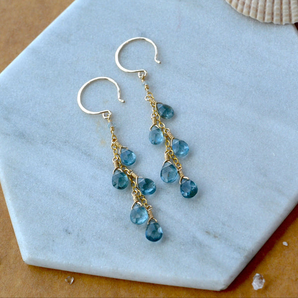 Gold dangling earrings with blue aquamarine gemstones on a marble surface