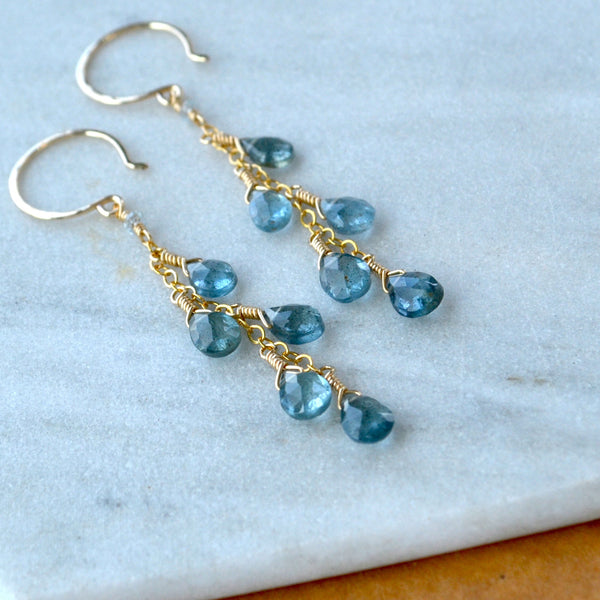Gold dangle earrings with blue aquamarine gemstones on a marble surface