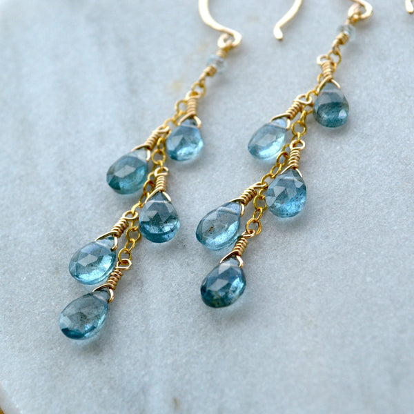 Gold earrings with blue aquamarine gemstones on a light marble background