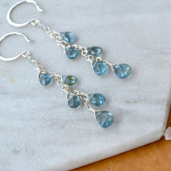 Blue aquamarine gemstone dangling earrings on a marble surface