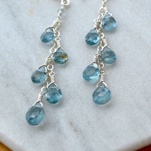 Silver dangle earrings with blue aquamarine gemstones on a marble surface