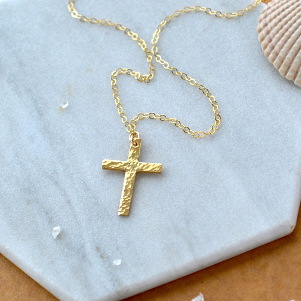 Gold cross necklace on a marble surface with a shell in the background