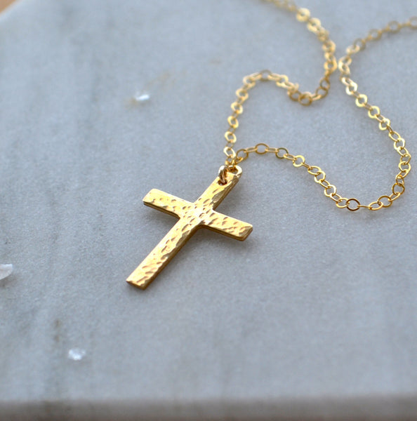 Gold cross necklace on a light gray background. hammered cross pendant