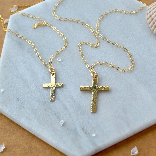 Two sizes of gold cross necklaces on a marble surface