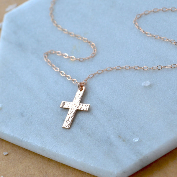 Rose gold cross necklace on a light blue stone surface