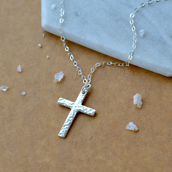 Silver cross necklace on a marble surface with small crystals around