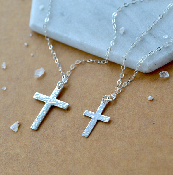 Two sizes of silver cross necklaces on a marble surface