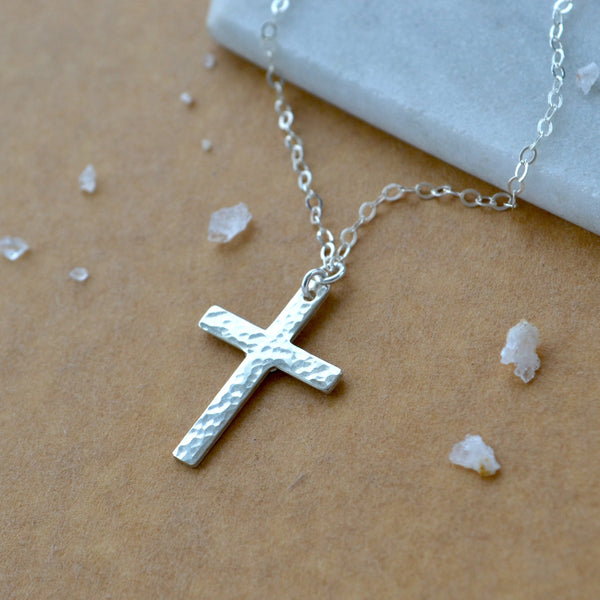 Silver cross necklace on a beige surface with small crystals