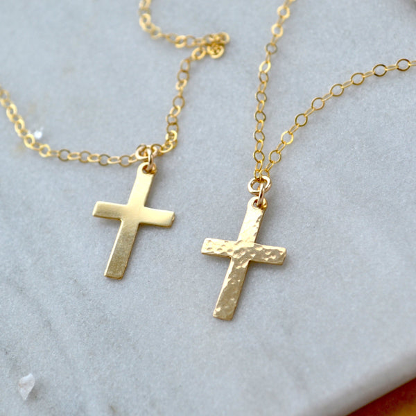 Gold cross necklaces on a marble surface hammered cross and smooth polished cross pendants
