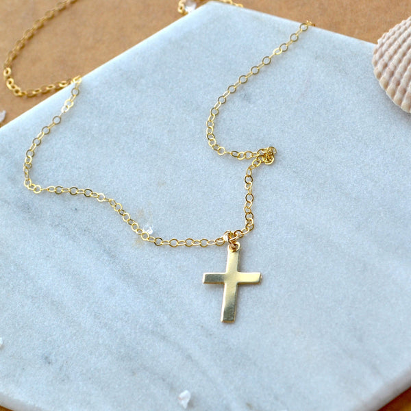 Gold necklace with a simple cross pendant on a white surface