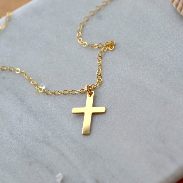 Small Gold cross necklace on a light gray surface