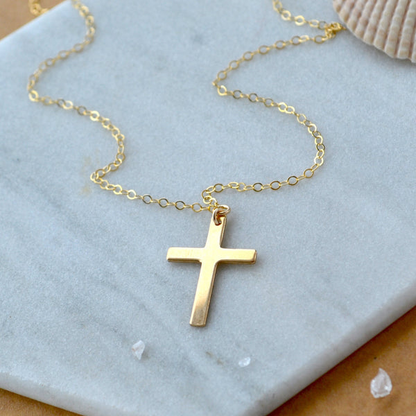 Gold plain cross necklace on a marble surface