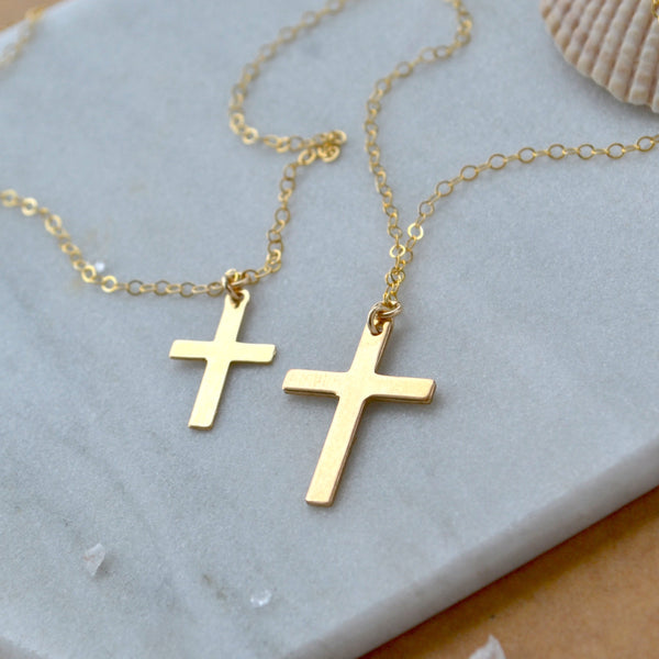 Two sizes of Gold cross necklace on a marble jewelry display