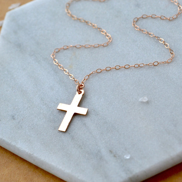 Rose gold cross necklace on a marble surface