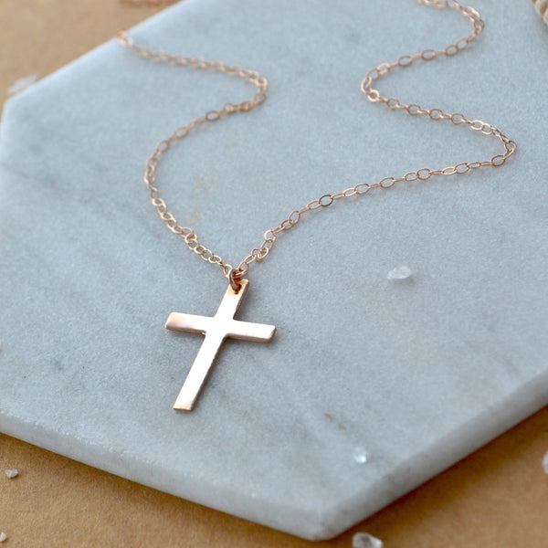 Rose gold cross necklace on a light blue stone surface