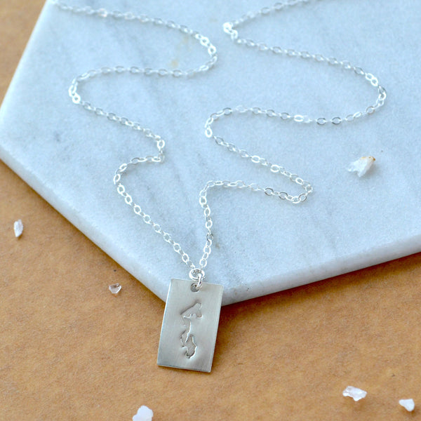 Silver necklace with a rectangle pendant featuring Whidbey Island on it. Displayed on a marble surface