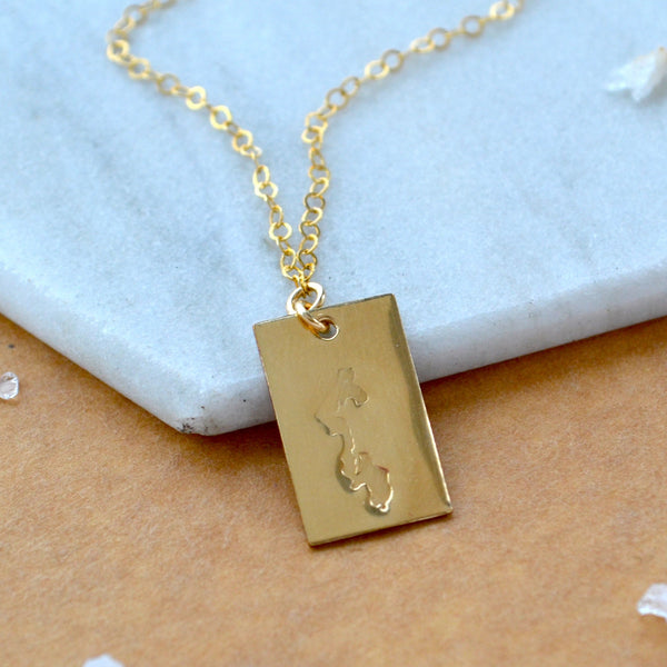 Gold necklace with a rectangular Whidbey Island pendant on a marble surface