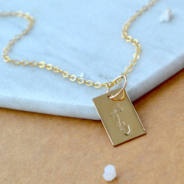 Gold necklace with a rectangular Whidbey Island pendant on a marble surface. Displayed with a simple chain made in custom sizes