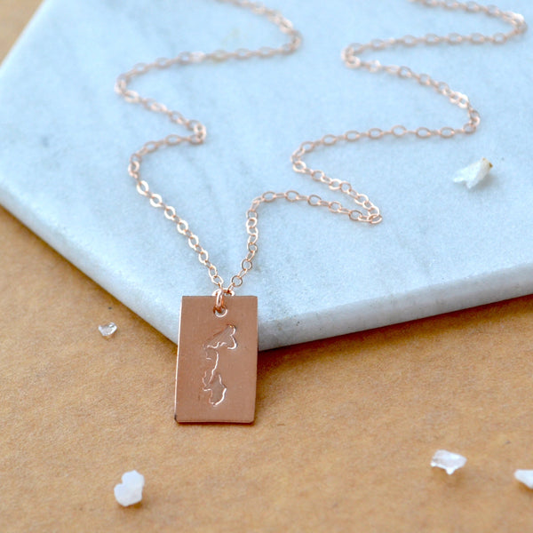 Rose gold necklace with a rectangular pendant of Whidbey Island on a marble surface