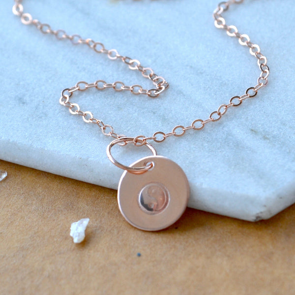 Rose gold necklace with a yin yang charm pendant on a brown and marble background