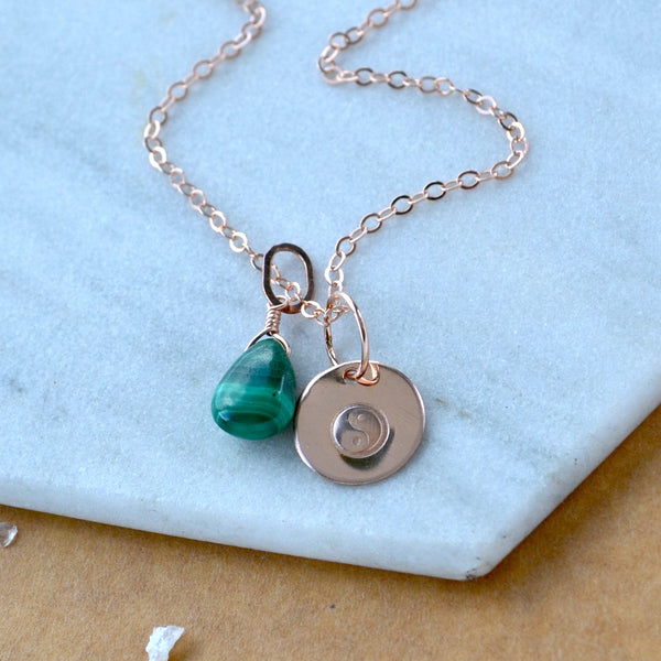 Necklace with green malachite teardrop pendant and yin yang charm on a light marble surface