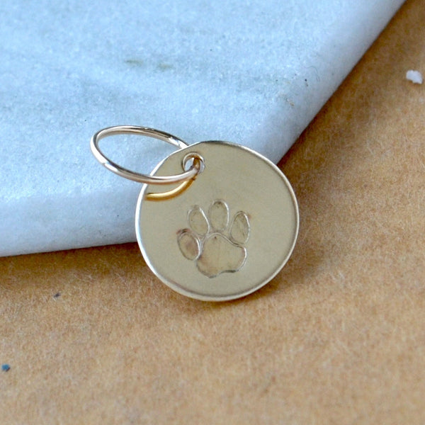 Gold Filled pet tag with paw print on a light marble and brown background