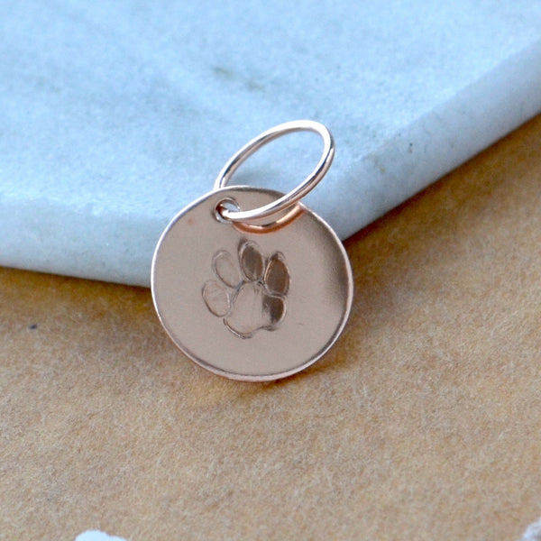 Rose gold dog paw print charm on a marble surface