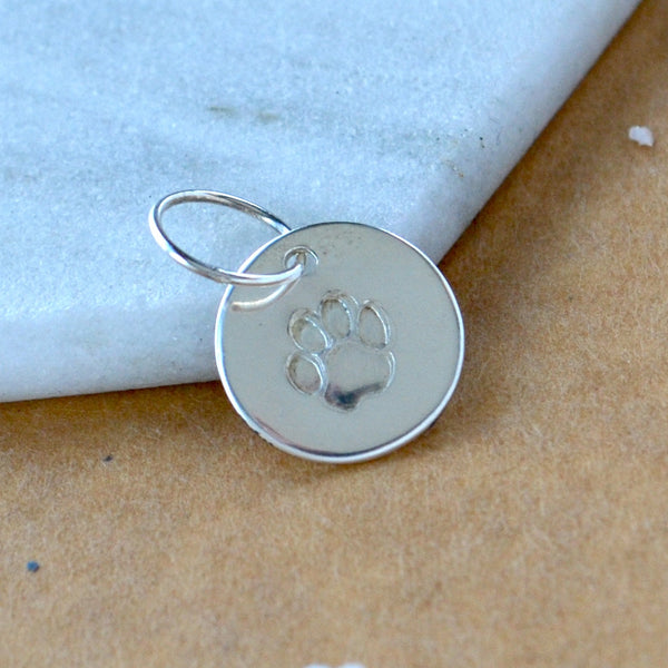 Silver round pendant with dog paw print design on a textured surface