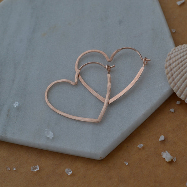 Rose gold heart-shaped earrings on a hexagonal stone with a shell and small stones on a brown background